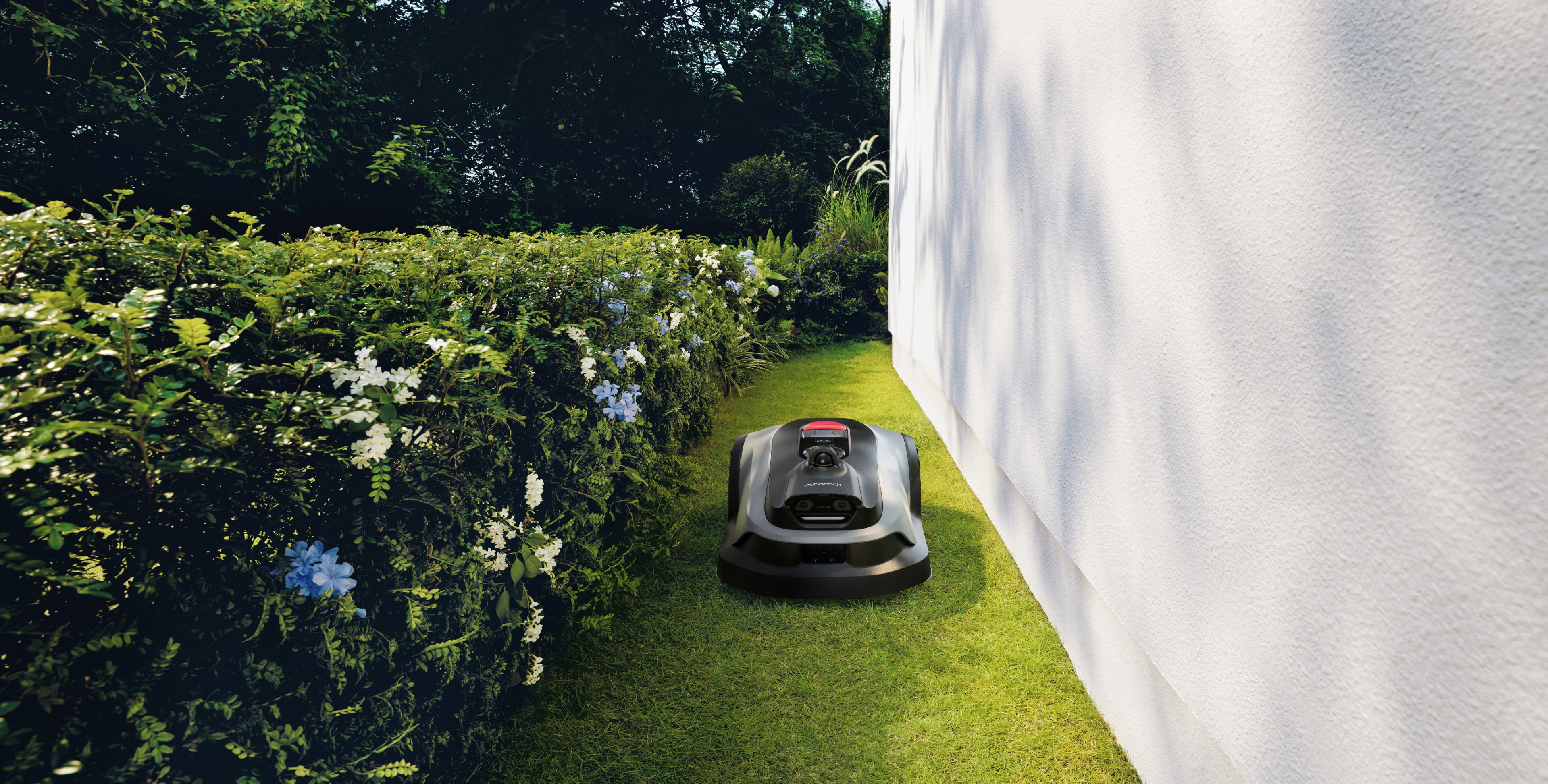 Compact robot mower traversing a tight 0.6 m passage between hedges and house wall