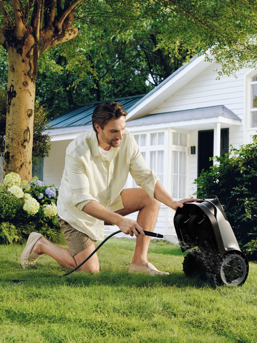 IPX6 water-resistant robotic lawn mower being washed down with a garden hose